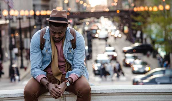 Man sitting with head down and hands clasped
